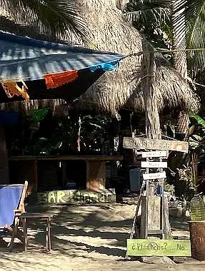 A rustic beach bar sits beneath palm shade, creating a relaxed beachfront retreat and casual afternoon escape along a Pacific Riviera getaway.