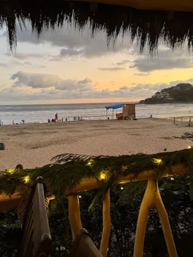 A sunset view overlooks the shoreline along the Nayarit Coast, with waves and scattered beachgoers beside an open stretch of water.