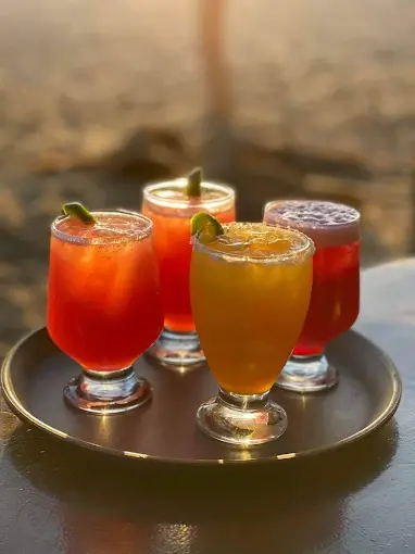 Four drinks on a tray at a Sayulita beach bar with lime garnishes and golden sunset light reflecting off the glasses near the ocean.