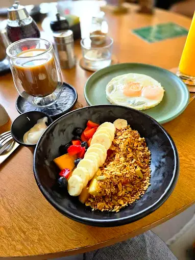 Granola and fresh fruit bowl with banana slices, berries, coffee, and fried eggs on a café table, showcasing breakfast at Sur 38 in Sayulita.