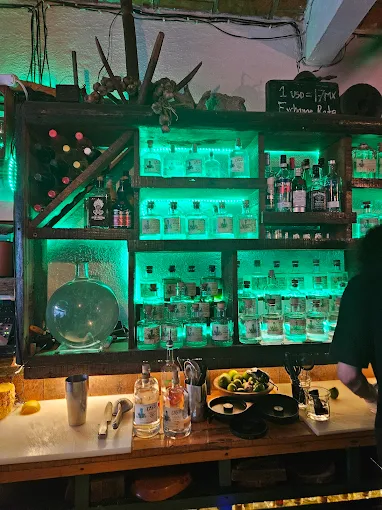 Back bar shelf in Sayulita illuminated with green lighting and stacked with tequila and mezcal bottles alongside citrus and bar tools.