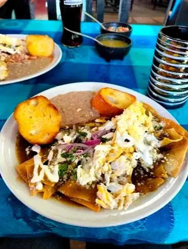 Hearty chilaquiles topped with scrambled eggs, cream, onions, and beans create a satisfying, traditional Mexican breakfast plate at Williams Restaurant