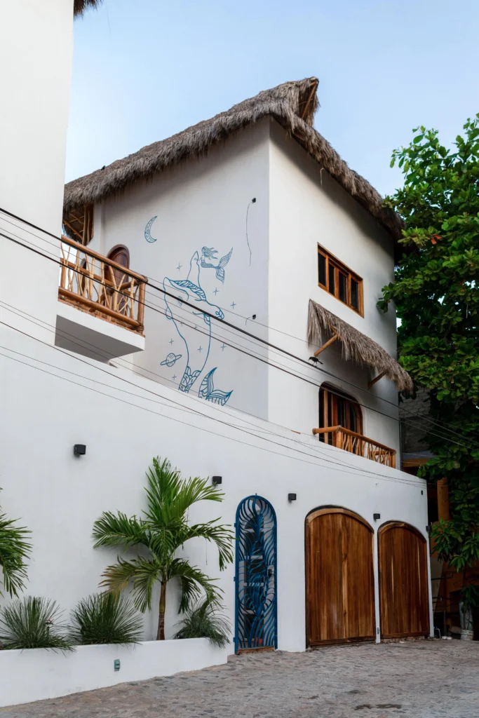 White hotel exterior with a hand-painted mural, thatched rooflines, and tropical plants at Amari Retreat in Sayulita, Nayarit.