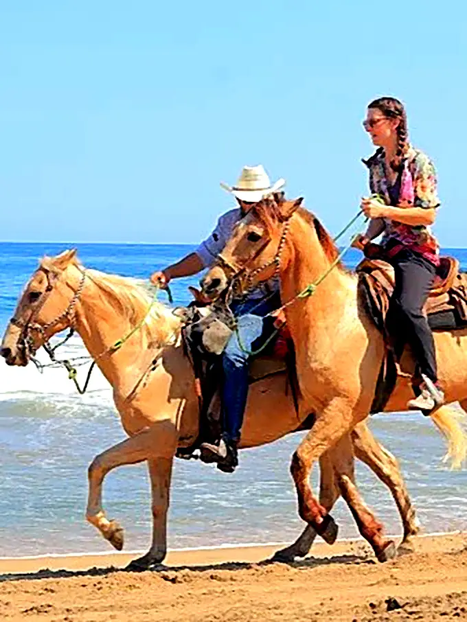 Two travelers horseback riding near the shoreline, highlighting a classic coastal experience in the Punta de Mita region.