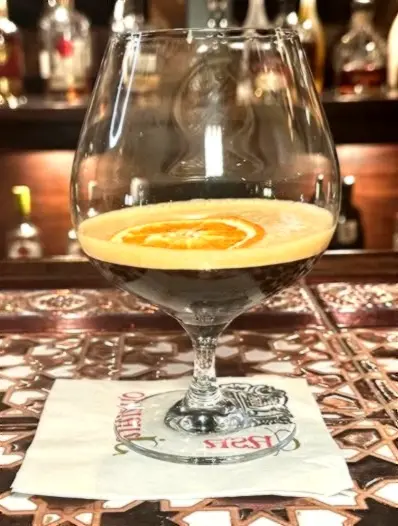 A creamy carajillo-style nightcap with orange garnish in a brandy glass, inspired by café culture and late dessert hours.