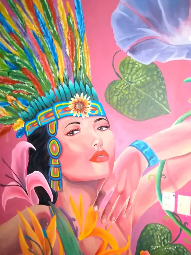 Vibrant mural of a woman in a colorful feathered headdress with tropical flowers and lush leaves, glowing with creative energy in the Nuevo Vallarta area.