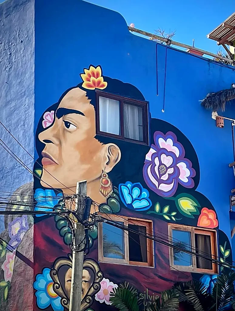 Striking Frida Kahlo mural painted on a vivid blue building with floral accents and windows, creating a bold moment on Nayarit’s Pacific coast.