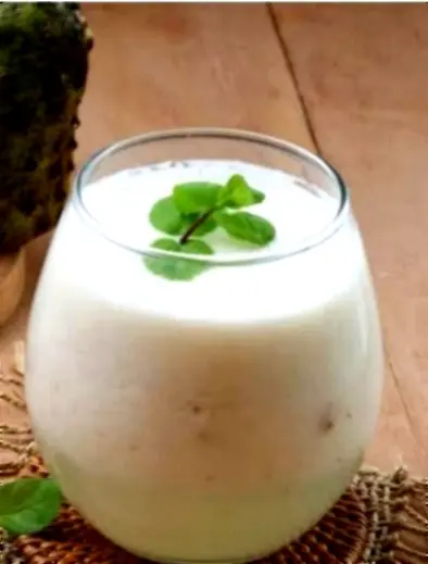 A creamy guanábana juice in a rounded glass with a mint sprig, offering smooth sweetness and cooling refreshment.