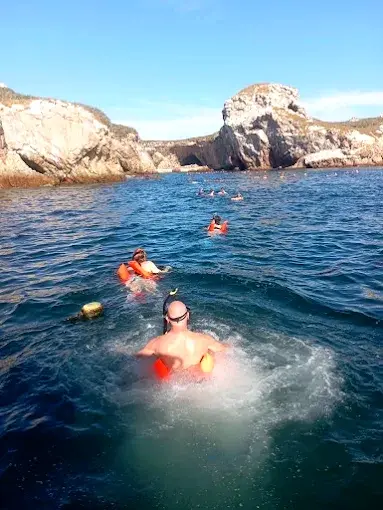 Swimmers in life vests spread across a calm cove with pale rock formations ahead, enjoying a guided swim in the Punta de Mita region.