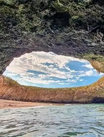 View from inside Hidden Beach looking up through the rocky opening to blue sky with scattered clouds at Las Islas Marietas National Park.