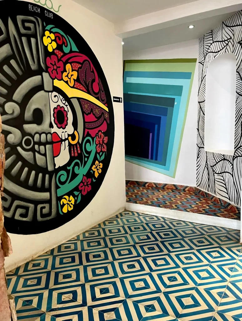 Huichol-inspired skull mural with bright floral details beside geometric tiles and layered color walls, forming a striking passageway in the Punta de Mita region.