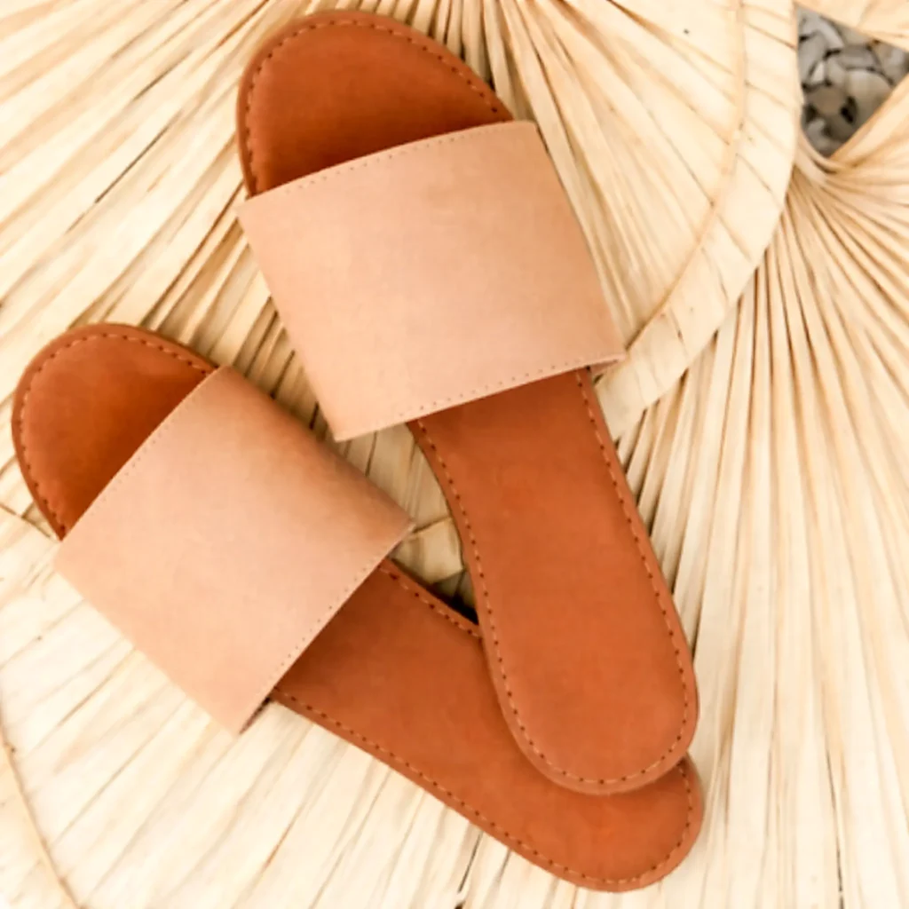 Minimalist tan slide sandals on a woven palm background, an easy packing pick for dinners and sunsets on the Costa Banderas.