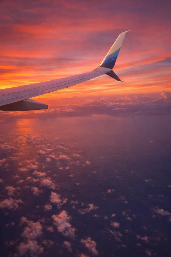 Airplane wing over the ocean at sunset, a travel-day reminder to pack essential medications and a small first-aid kit.
