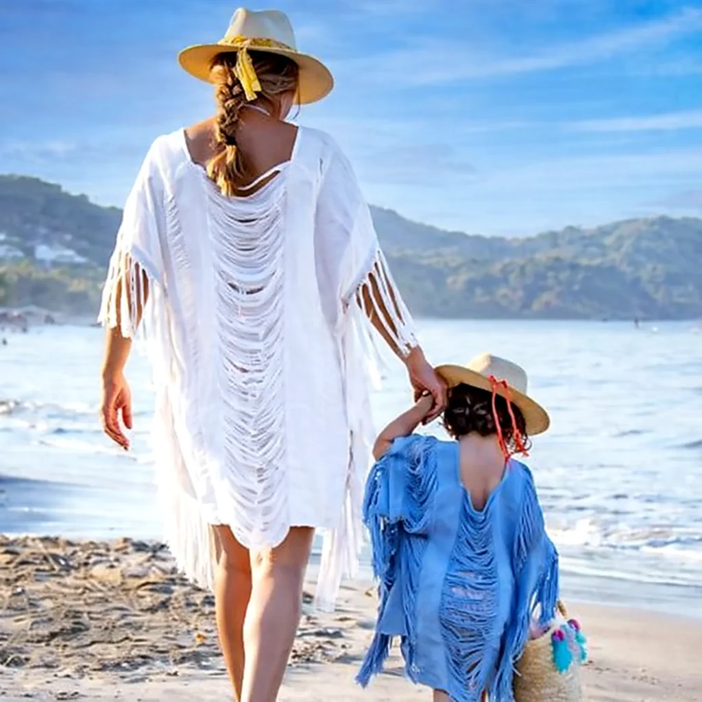 Mom and daughter in fringe beach coverups and sun hats walking along the shoreline with mountains in view in the Punta de Mita region.