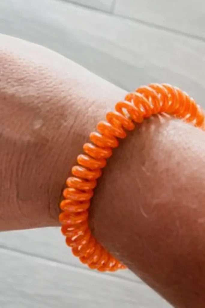 Close-up of an orange spiral mosquito repellent bracelet on a wrist, a simple comfort for breezy evenings, dinners outside, and patio lounging.