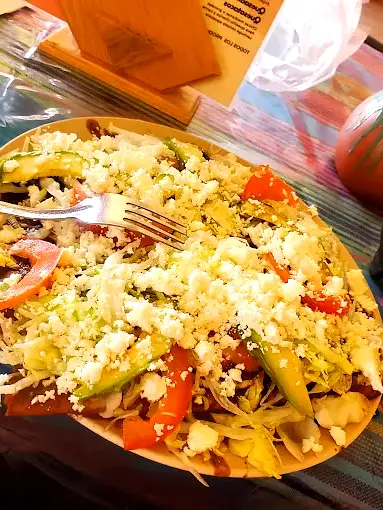Oaxacan tlayuda topped with beans, cheese, tomatoes, avocado, and lettuce on a crisp tortilla.
