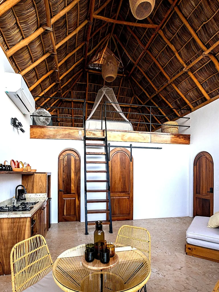 Amari’s loft suite featuring a thatched palapa roof, cozy upstairs bed, handmade accents, and a welcoming open layout designed for coastal living.
