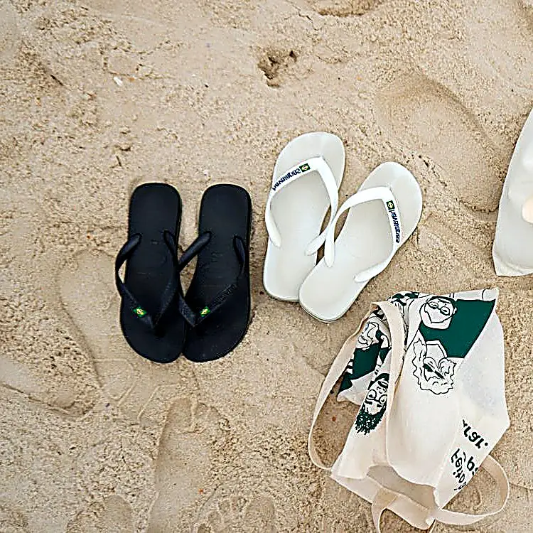 White and black flip-flops on sand beside a reusable tote bag, easy essentials for relaxed beach days on the Pacific coast of Nayarit.