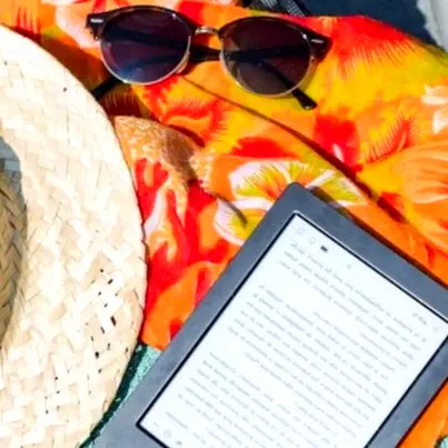 E-reader on a colorful beach towel beside sunglasses and a straw hat, perfect for relaxing reading time on Nayarit’s Pacific coast.