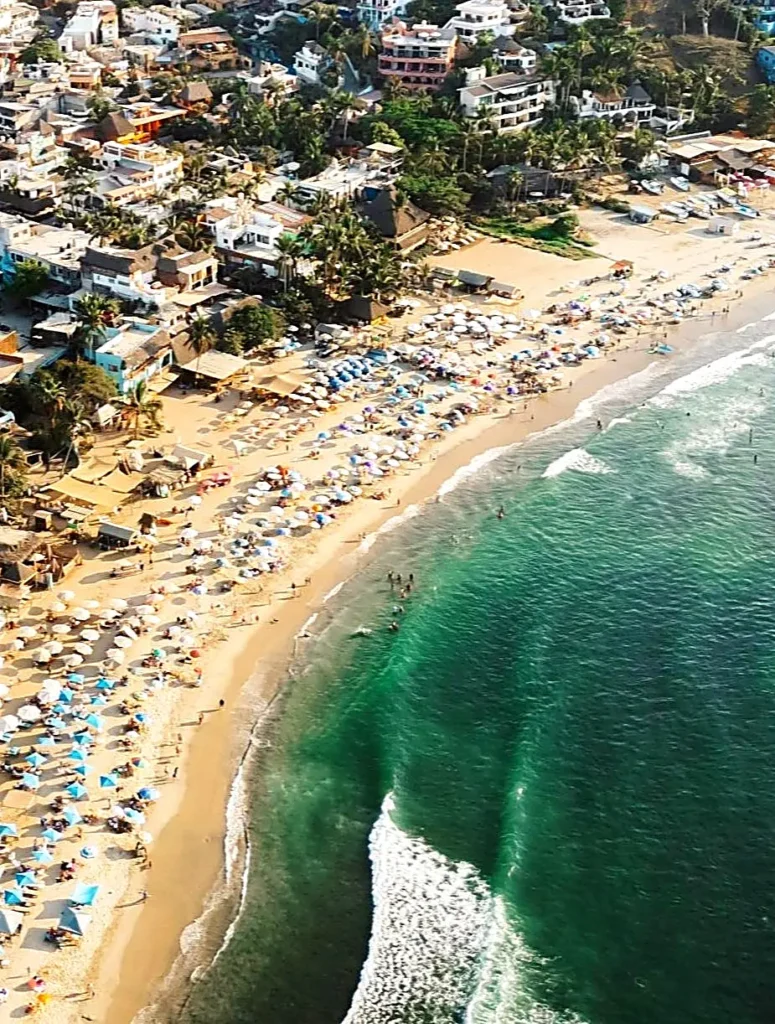 Aerial view of Sayulita’s main beach lined with umbrellas and town buildings, capturing the lively vibe in the Punta de Mita region.