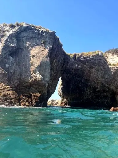 Rock sea arch with a narrow cave opening above turquoise water, photographed from the surface at the Marietas Islands.