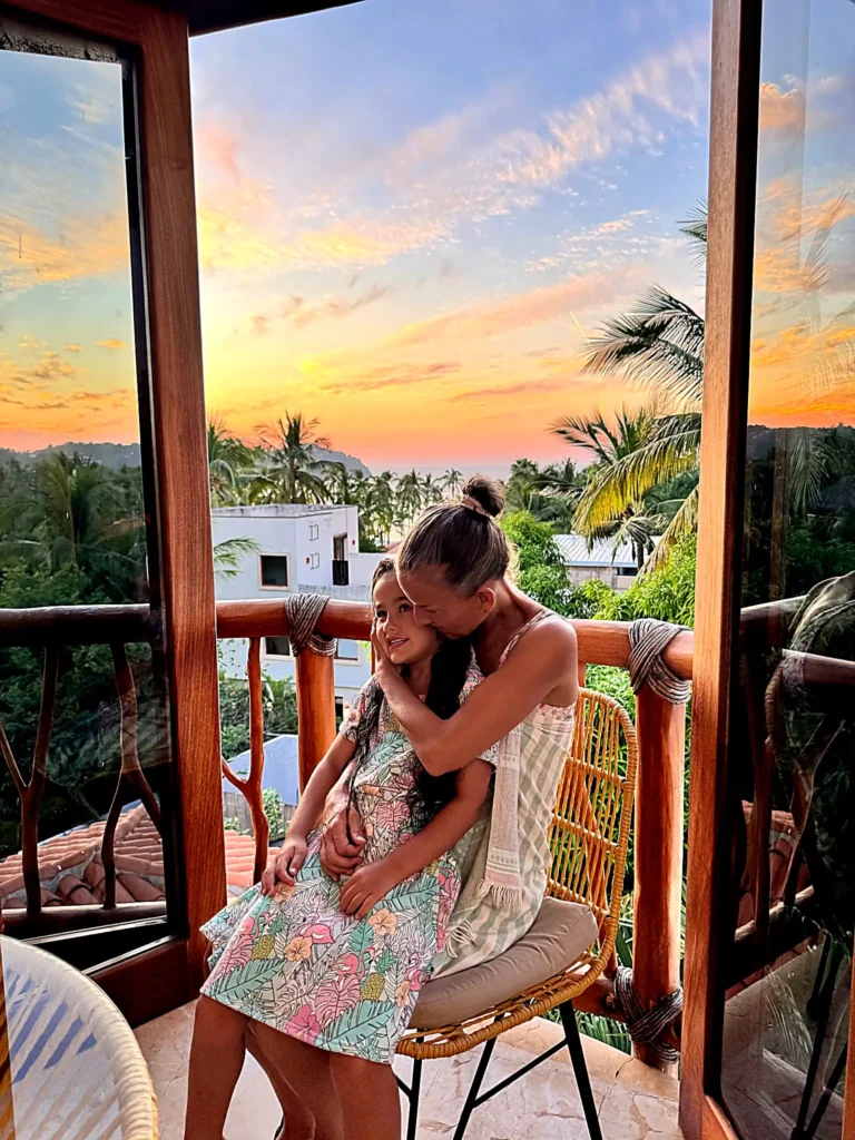 A parent and child share a warm sunset moment on a private balcony at Amari Boutique Hotel in Sayulita, surrounded by ocean colors in the evening sky.