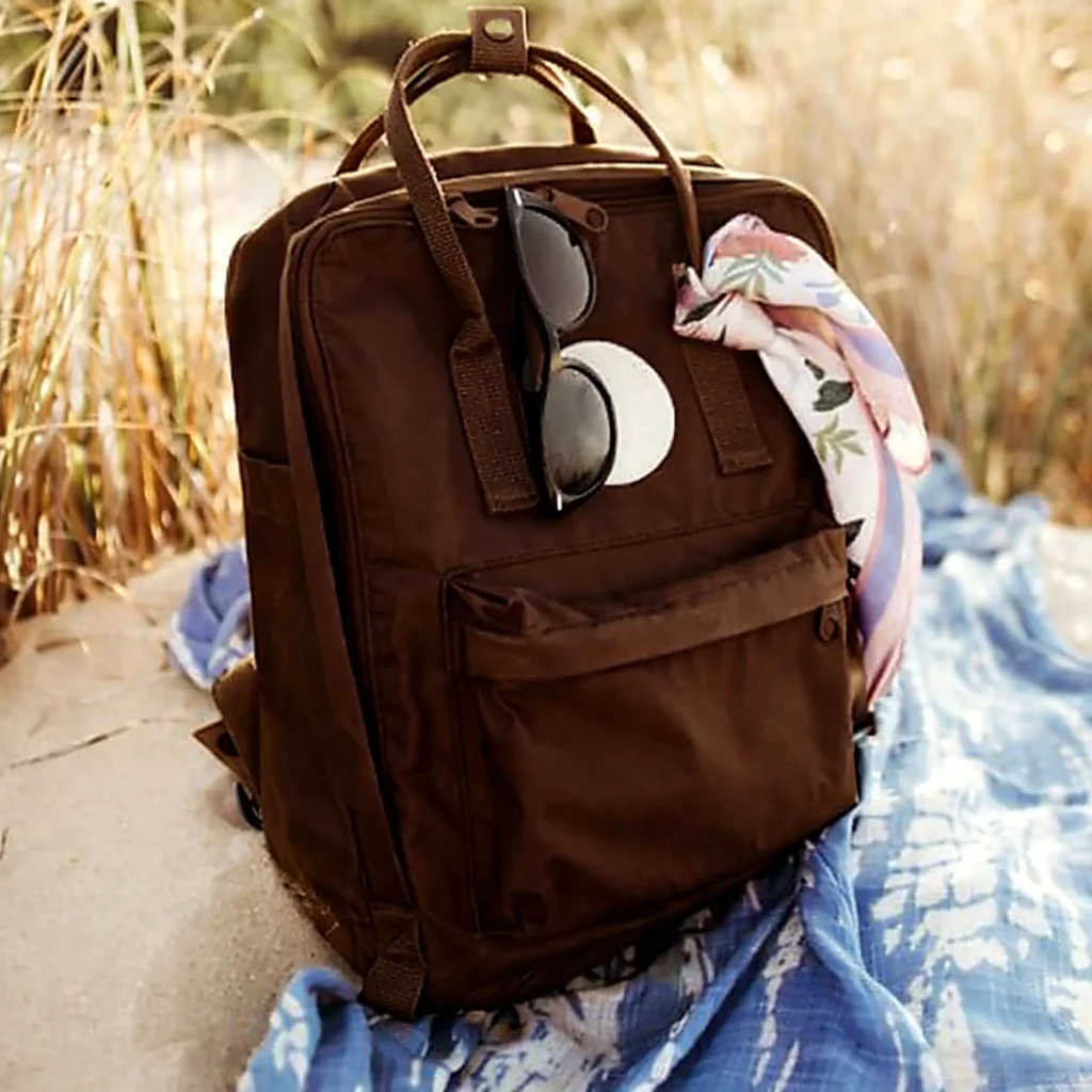 Brown daypack with sunglasses and a patterned scarf resting on a beach blanket, an easy carry for exploring Sayulita.