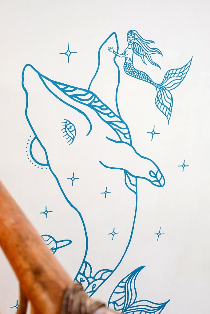 Minimal line-art mural of a whale with a mermaid above, surrounded by tiny stars, creating a playful ocean detail at Amari Boutique Hotel.