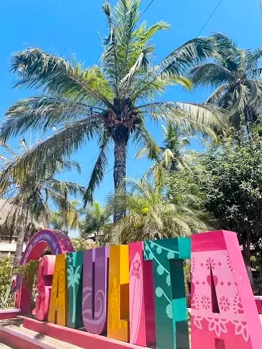 Colorful town landmark surrounded by palm trees and visitors gathering in the central plaza.