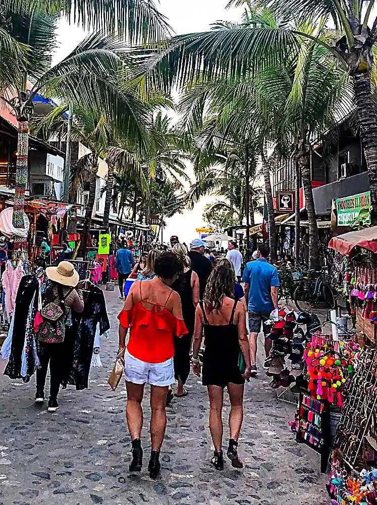 Visitors stroll along a palm-lined street in downtown Sayulita surrounded by colorful shops, artisan vendors, restaurants, and local businesses.