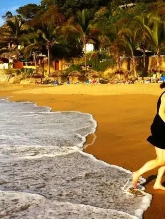 Una persona camina descalza por la orilla de Playa Sayulita mientras suaves olas del Pacífico llegan a la arena dorada.