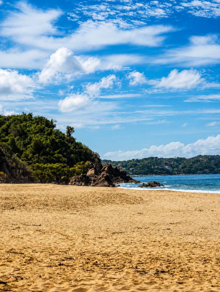 Quiet golden-sand beach with a green headland and hillside homes across the bay in Sayulita, Nayarit, Mexico